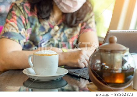 Hot Cappuccino coffee for quarantined woman wear face mask and work from home by using tablet and stress relief with hot coffee. Concepts of Covid-19 (Coronavirus disease). Selective focus on coffee. Hot Cappuccino coffee for quarantined woman wear face mask and work from home by using tablet and stress relief with hot coffee. Concepts of Covid-19 (Coronavirus disease). Selective focus on coffee. 83562872