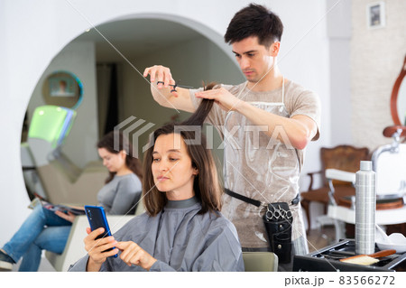 Girl client using phone during hair cut by professional hairdresser 83566272