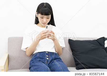 ソファーに座りうつむき加減でスマホを操作する若い女性 83567144