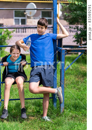 teenage boy and girl exercising outdoors, sports ground in the yard, they posing at the horizontal bar, healthy lifestyle 83569291