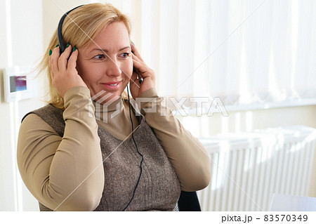 Smiling middle-aged caucasian woman puts on a headset. Copy space. 83570349