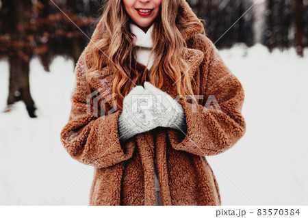 Beautiful young woman in snowy fancy winter woodland. Girl wearing fluffy gloves, cap and coat. Christmas forest, trees on blurred background. Crossed hands because of cold weather. High quality photo Beautiful young woman in snowy fancy winter woodland. Girl wearing fluffy gloves, cap and coat. Christmas forest, trees on blurred background. Crossed hands because of cold weather. High quality photo 83570384
