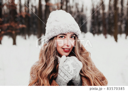 Beautiful young woman in snowy fancy winter woodland. Girl wearing fluffy gloves, cap and coat. Christmas forest, trees on blurred background. Crossed hands because of cold weather. High quality photo Beautiful young woman in snowy fancy winter woodland. Girl wearing fluffy gloves, cap and coat. Christmas forest, trees on blurred background. Crossed hands because of cold weather. High quality photo 83570385