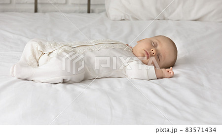 Cute baby in white bodysuit sleeping on comfortable bed Cute baby in white bodysuit sleeping on comfortable bed 83571434