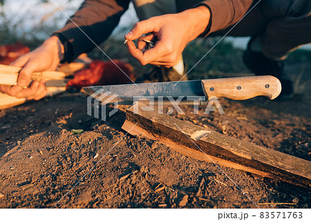 Man chops wood with a large bonfire knife on a sunny day. 83571763
