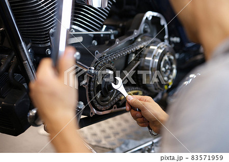 A man spins a part on a motorcycle with a wrench A man spins a part on a motorcycle with a wrench 83571959