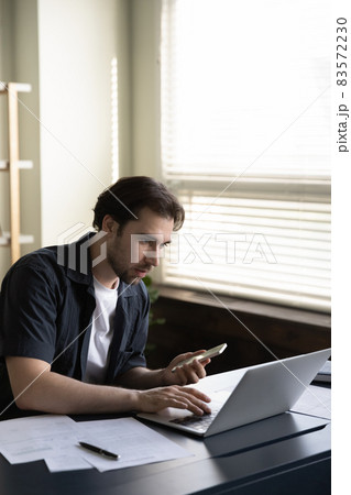 Vertical image concentrated young businessman using different gadget. Vertical image concentrated young businessman using different gadget. 83572230