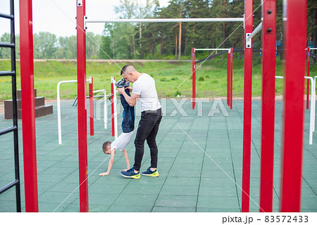 Caucasian man teaching son handstand at playground. 83572433