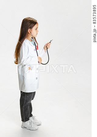 Side view. Cute beautiful little girl, child in image of doctor wearing white lab coat posing isolated on white studio background 83573895