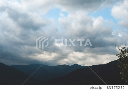 Thick white clouds over mountains covered with green forest Thick white clouds over mountains covered with green forest 83575232