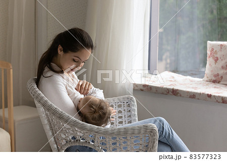 Loving young mom breastfeeding little daughter, sitting in chair 83577323