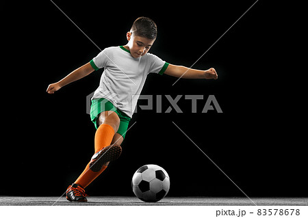 Full-length portrait of boy, child, football player in uniform training isolated over black background. Full-length portrait of boy, child, football player in uniform training isolated over black background. 83578678