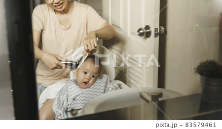 Asian Young Mother cutting and trimming her little baby son hair in bathroom at home. 83579461