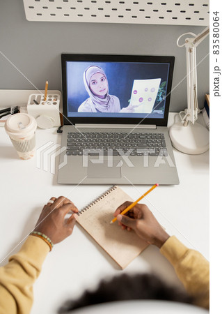 Hands of student making notes in front of laptop 83580064
