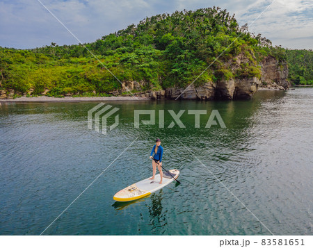 Young women Having Fun Stand Up Paddling in the sea. SUP. Red hair girl Training on Paddle Board near the rocks 83581651