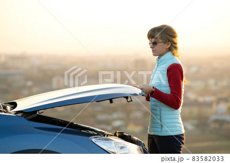 Young woman opening bonnet of broken down car having trouble with her vehicle. Female driver near auto with popped up hood. Young woman opening bonnet of broken down car having trouble with her vehicle. Female driver near auto with popped up hood. 83582033
