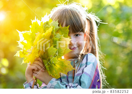 Portrait of happy pretty child girl holding a bunch of fallen tree leaves in autumn forest. Positive female kid enjoying warm day in fall park. 83582252