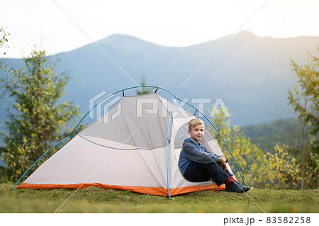Happy hiker child boy resting in a tourist tent at mountain campsite enjoying view of beautiful summer nature. 83582258