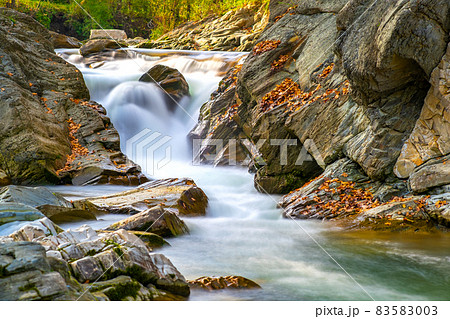 Mountain river with small waterfall with clear turquoise water falling down between wet boulders with thick white foam on autumn bright day. Mountain river with small waterfall with clear turquoise water falling down between wet boulders with thick white foam on autumn bright day. 83583003