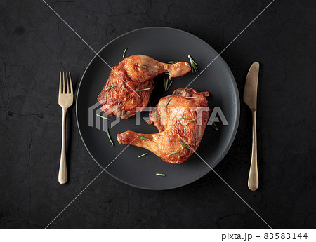 Grilled chicken leg sprinkled with rosemary on a black plate. 83583144