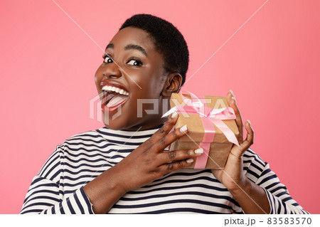Excited Overweight Black Female Holding Gift Box On Pink Background Excited Overweight Black Female Holding Gift Box On Pink Background 83583570