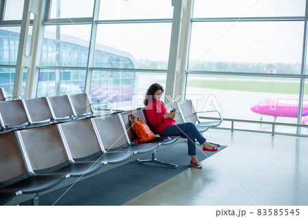 A girl is sitting on an empty row of seats in front of a large stained glass window in an airport terminal, waiting for a flight A girl is sitting on an empty row of seats in front of a large stained glass window in an airport terminal, waiting for a flight 83585545