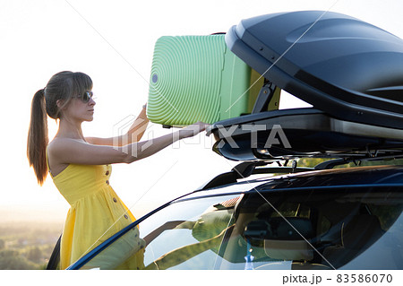 Young woman taking green suitcase from car roof rack. Travel and vacations concept. 83586070
