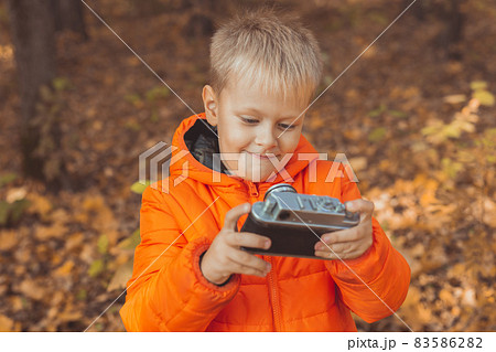Boy with retro camera taking pictures outdoor in autumn nature. Leisure and photographers concept Boy with retro camera taking pictures outdoor in autumn nature. Leisure and photographers concept 83586282