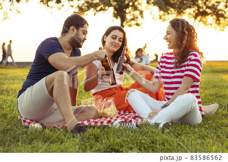 Three friends sitting on the grass in the park Three friends sitting on the grass in the park 83586562