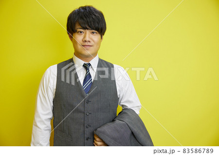 黄色い背景の前で爽やかに笑うスーツを着た日本人男性	 83586789
