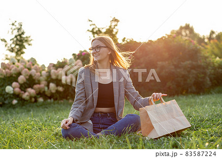 Hungy Caucasian businesswoman, student or freelancer with craft paper bag siting in the park, ordering takeaway food delivery. Concept of rest and break on job. Hungy Caucasian businesswoman, student or freelancer with craft paper bag siting in the park, ordering takeaway food delivery. Concept of rest and break on job. 83587224
