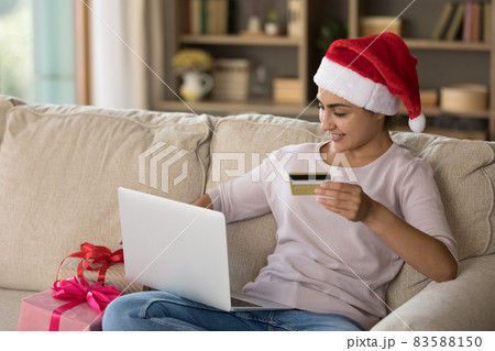 Happy beautiful young Indian woman purchasing Christmas gifts online. 83588150