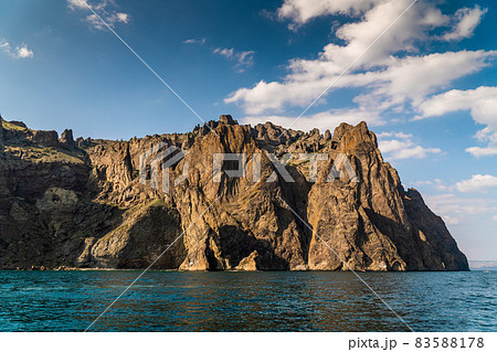 The Crimean Peninsula. July 21, 2021. A picturesque and mysterious view of high rocks on Cape Karagach near the city of Koktebel from the Black Sea. The Crimean Peninsula. July 21, 2021. A picturesque and mysterious view of high rocks on Cape Karagach near the city of Koktebel from the Black Sea. 83588178