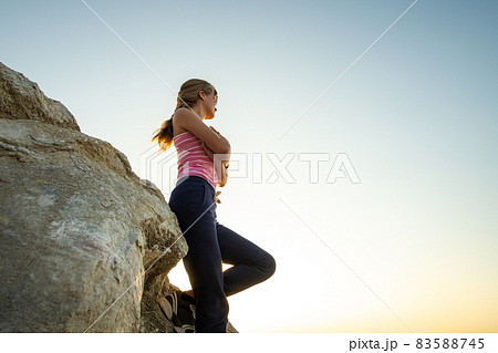 Woman hiker leaning on a big rock enjoying warm summer day. Young female climber resting during sports activity in nature. Active recreation in nature concept. 83588745