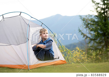 Happy child boy resting alone in a tourist tent at mountain campsite enjoying view of beautiful summer nature. Hiking and active way of life concept. Happy child boy resting alone in a tourist tent at mountain campsite enjoying view of beautiful summer nature. Hiking and active way of life concept. 83588929