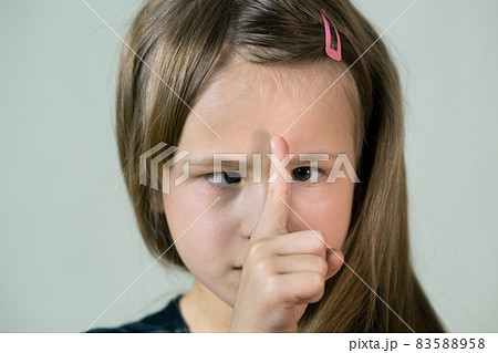 Close-up portrait of happy smiling little girl with long hair looking with crossed eyes at her point finger. Close-up portrait of happy smiling little girl with long hair looking with crossed eyes at her point finger. 83588958