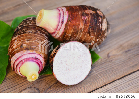 Taro root with half slice on taro leaf and wooden background, Fresh raw organic taro root ready to cook Taro root with half slice on taro leaf and wooden background, Fresh raw organic taro root ready to cook 83593056