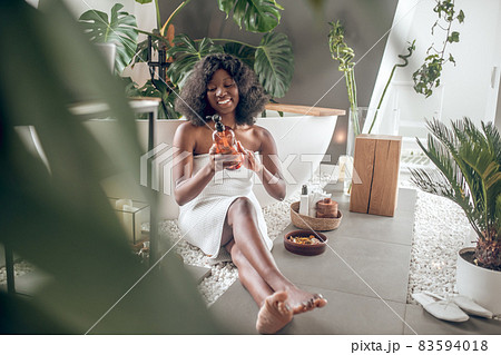 Pretty dark-skinned woman civered with towel choosing body lotion Pretty dark-skinned woman civered with towel choosing body lotion 83594018
