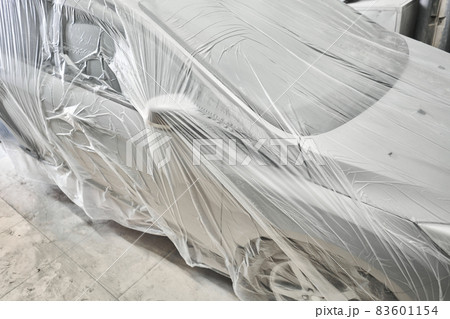 Garage painting car service. section of the car is covered with primer. vehicle is covered with protective paper. Repairing car body work after the accident by working sanding primer before painting. 83601154