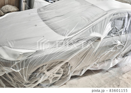 Garage painting car service. section of the car is covered with primer. vehicle is covered with protective paper. Repairing car body work after the accident by working sanding primer before painting. 83601155