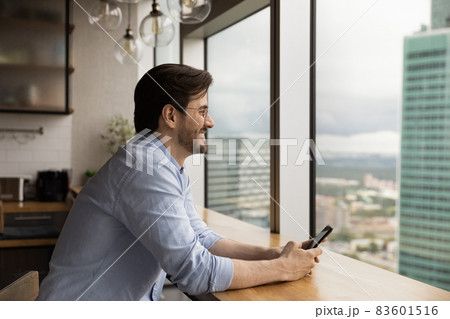 Dreamy happy young caucasian man holding cellphone in hands. Dreamy happy young caucasian man holding cellphone in hands. 83601516