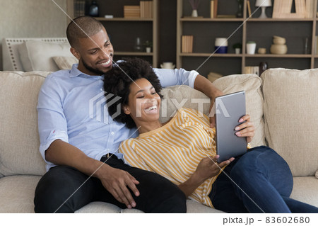 Relaxed smiling millennial mixed race couple using tablet. 83602680