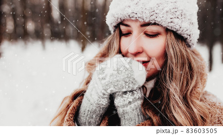Beautiful young woman in snowy fancy winter woodland. Girl wearing fluffy gloves, cap and coat. Christmas forest, trees on blurred background. Crossed hands because of cold weather. High quality photo Beautiful young woman in snowy fancy winter woodland. Girl wearing fluffy gloves, cap and coat. Christmas forest, trees on blurred background. Crossed hands because of cold weather. High quality photo 83603505