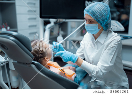 Side view of dentist in medical uniform who treats teeth of little girl patient in dental office Side view of dentist in medical uniform who treats teeth of little girl patient in dental office 83605261