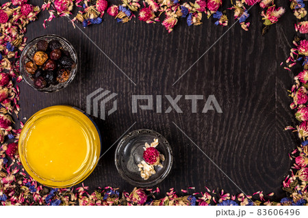 Organic honey in a small jar, mud and clay powder on wooden background. Frame of dried flowers 83606496
