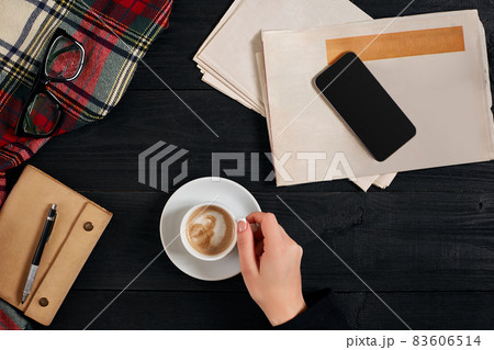 Newspaper and smartphone, reading glasses, notebook, hands holding coffee cup. 83606514