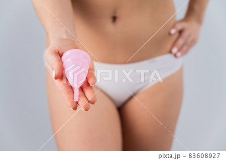 Close-up of a woman in white cotton panties holding a pink menstrual cup against a white background. Alternative to tampons and pads 83608927