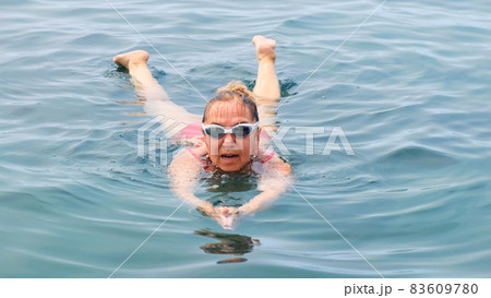 female in glasses and a red swimsuit is practicing crawl swimming in the sea. Professional swimmer female in glasses and a red swimsuit is practicing crawl swimming in the sea. Professional swimmer 83609780