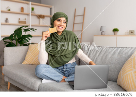 Arab lady in hijab using credit card for remote payment, shopping online via laptop, buying goods in web store at home 83616076