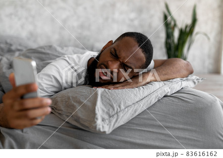 Black man suffering from insomnia looking at phone in bed Black man suffering from insomnia looking at phone in bed 83616162